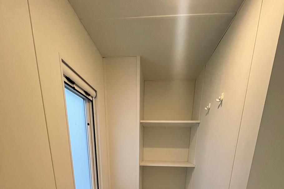 Bagno stretto con wc, bidet, scaffali e finestra, pavimento in legno.