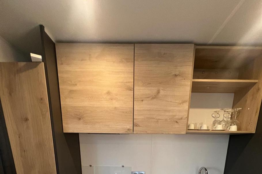 Piccola cucina moderna con frigorifero, piano cottura, lavello e armadietti in legno chiaro.