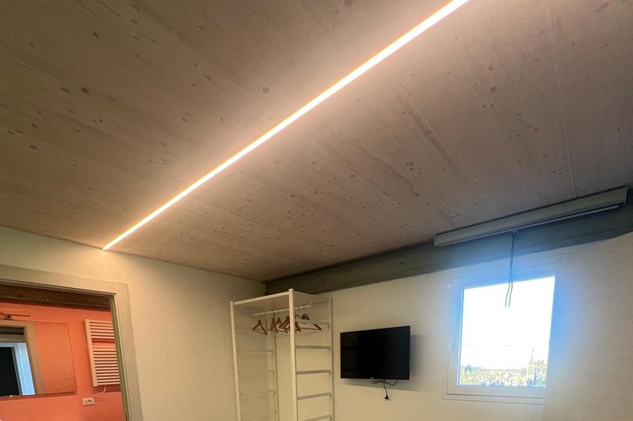 Camera moderna con letto matrimoniale, TV a parete, armadio aperto e bagno adiacente.